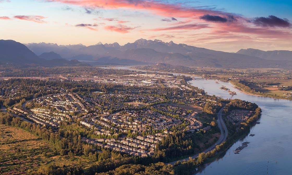 an arial image of a community beside a river with mountains in the distance