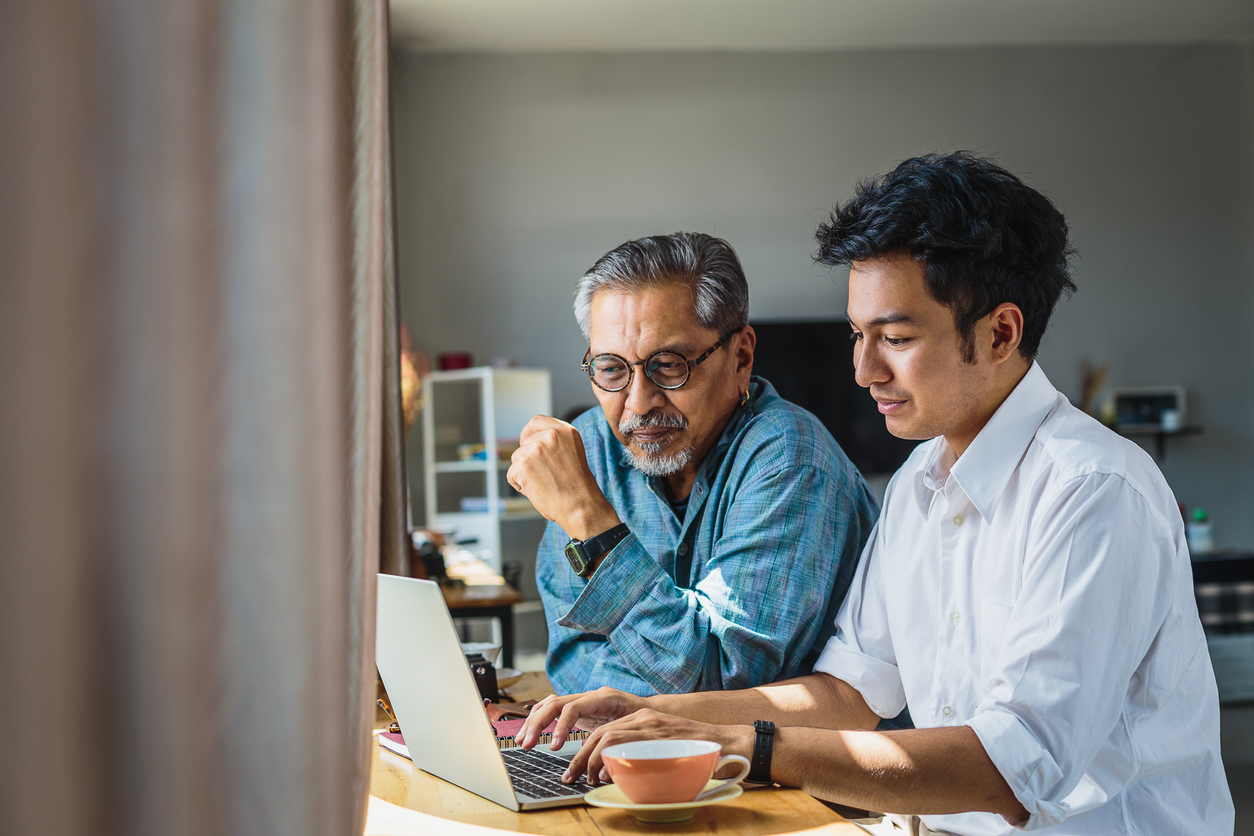 Older and younger men sitting at desk with laptop computer