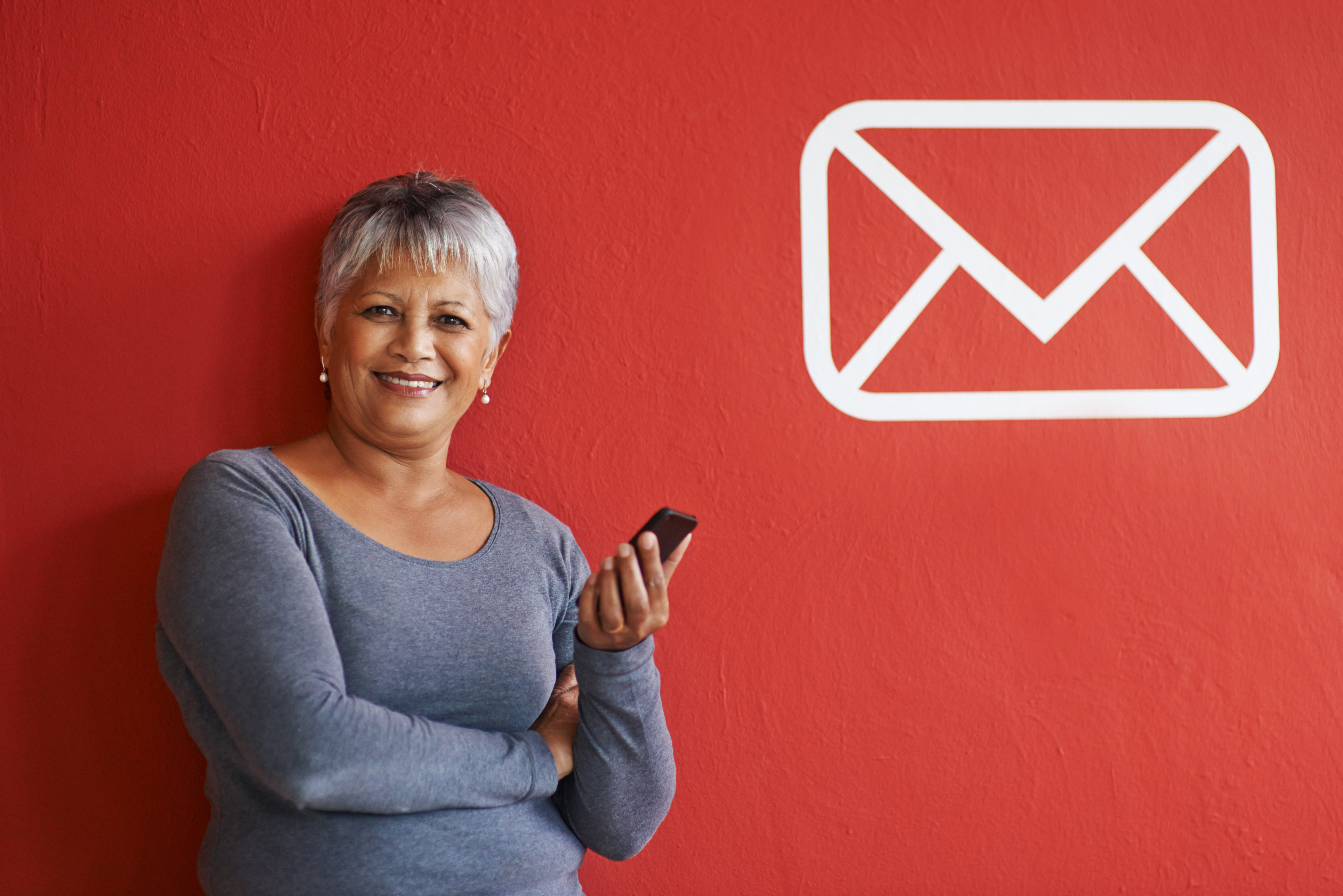 Woman with mobile phone on red background with mail icon on wall.